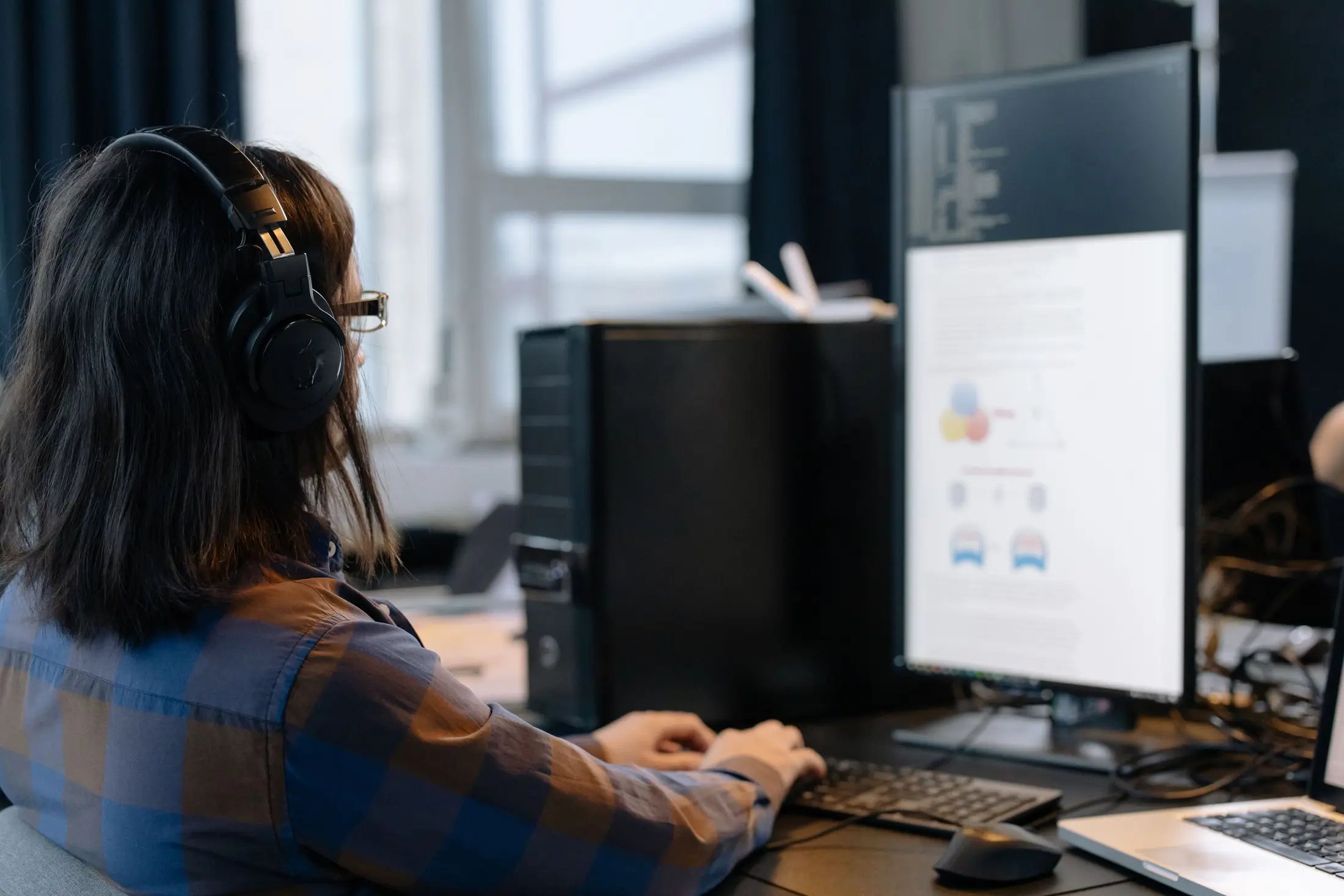 An IT specialist with headphones working at a desk with a large screen